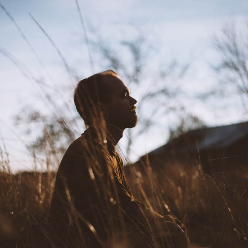 A man standing in a field, taking a deep breath and appearing relaxed. This image represents the practice of grounding and using breath and nature to reduce stress and anxiety in Orange County California.