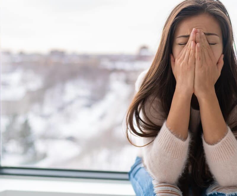 A woman holding her hands to her face, appearing anxious or stressed. This image represents a common emotion that can be managed through grounding techniques.