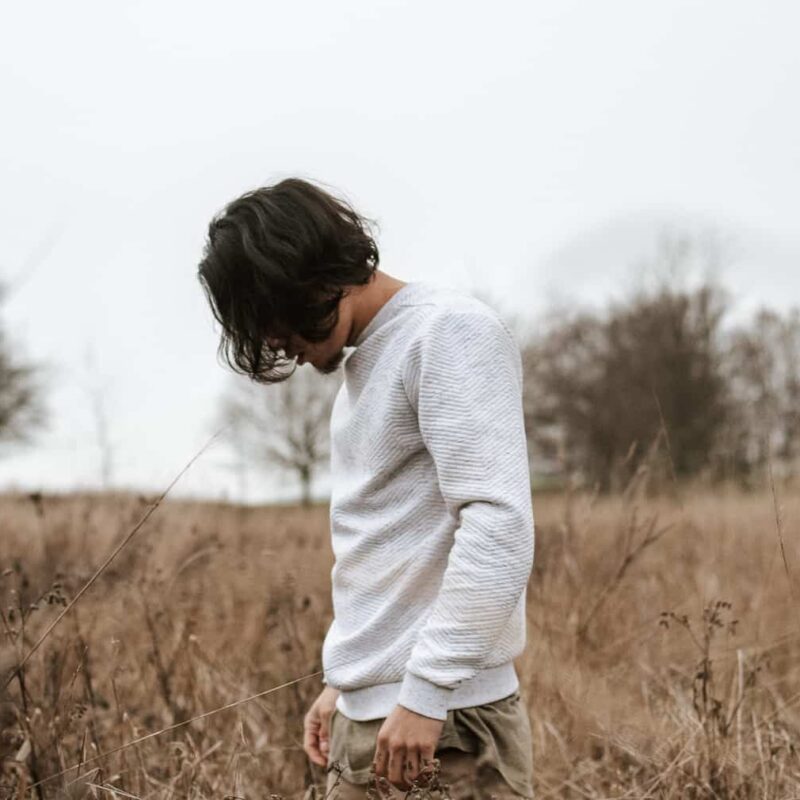 A man standing alone in an open field, looking down introspectively - representing the contemplative and healing journey taken during Dialectical Behavior Therapy.