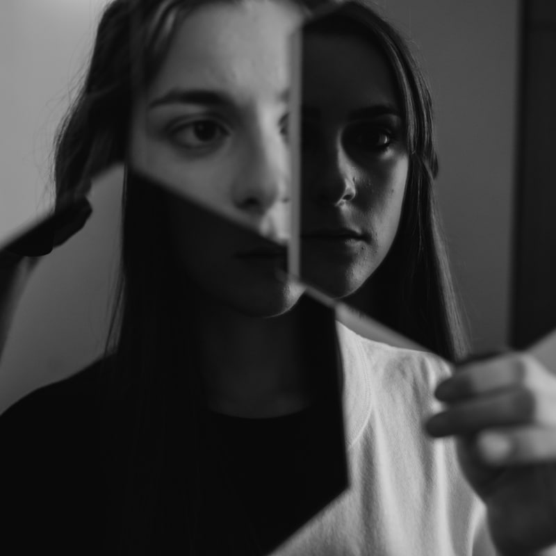 A woman holds two mirrors reflecting her face. Symbolic representation of self-reflection, exploring Schizoid and Schizotypal Personality Disorders