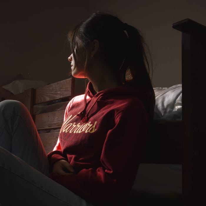 Young woman sitting in a dark room, looking away from the camera, reflecting feelings of unspecified depressive disorder and introspection.