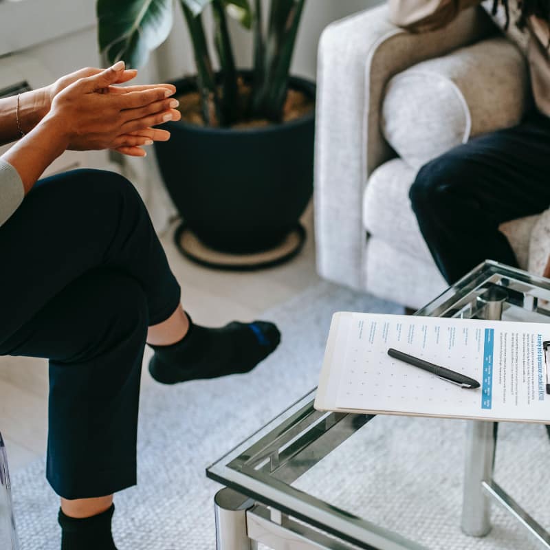 A man sitting on a couch engaged in conversation with a therapist, creating a safe space for open dialogue and personal exploration in narrative therapy.