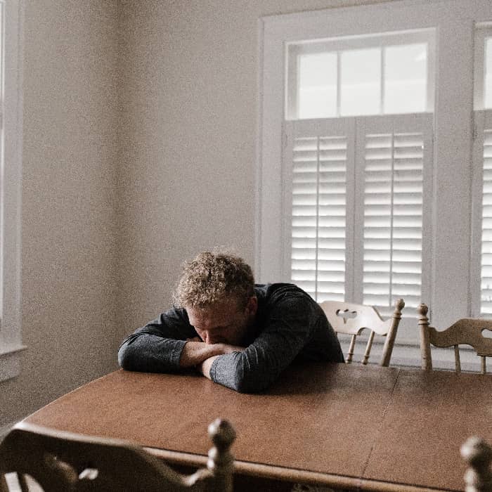 A man with his head down on the table, signifying struggle with negative thinking and cognitive distortions.