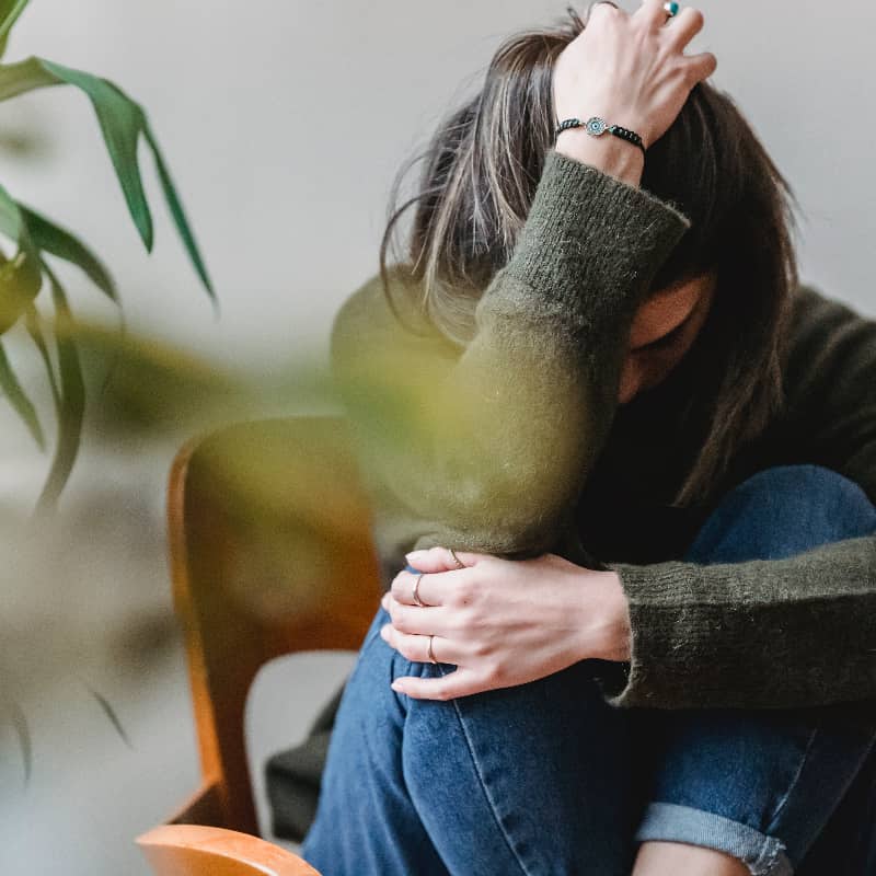 A woman sitting on the ground, covering her head, representing the emotional weight and struggle associated with despair.