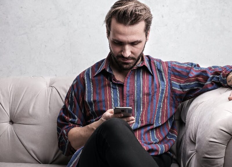 Man intently viewing his phone on a couch, representing the influence of social media on depression.