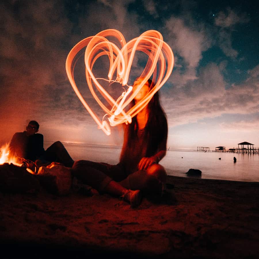 Blurry woman drawing a light heart in the air, symbolizing the often obscured signs of a codependent relationship.