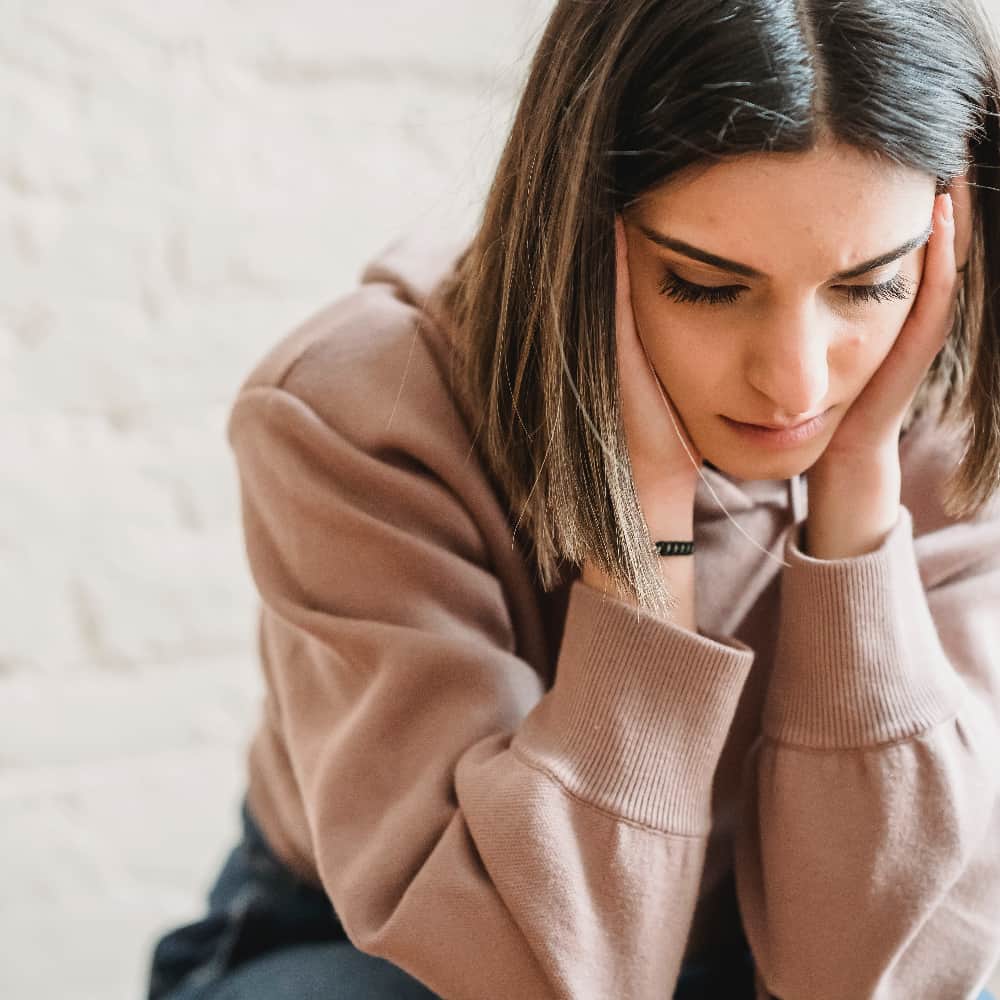 A woman holding her face with a pensive expression, symbolizing the impact of negative self-talk on self-esteem.