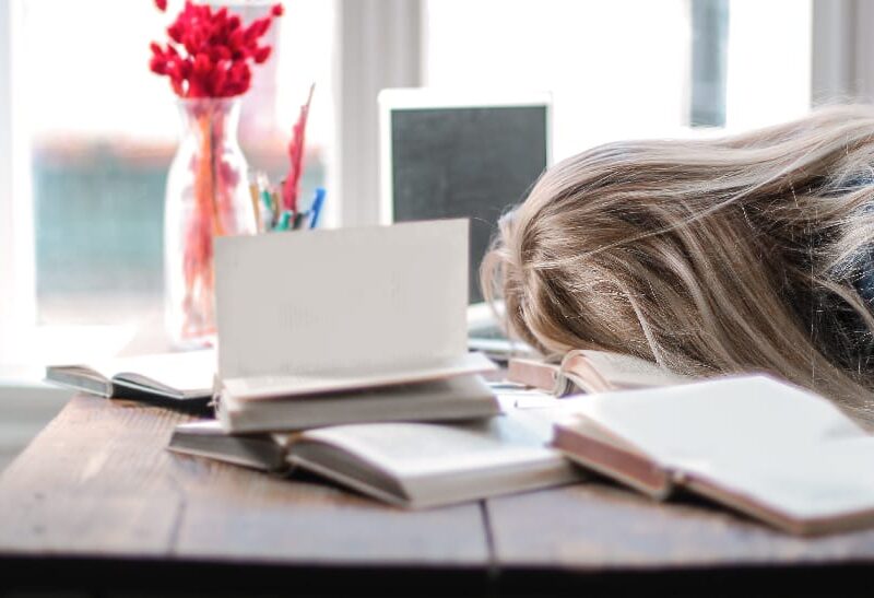 Exhausted woman laying face down on her desk, showcasing evident signs of stress and mental fatigue.