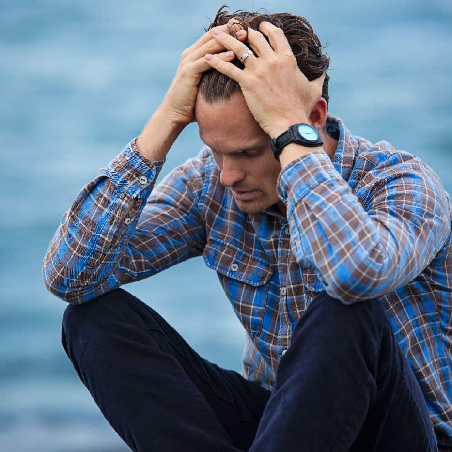 Despondent man standing by the water's edge, reflecting on mental health IOP options near him.