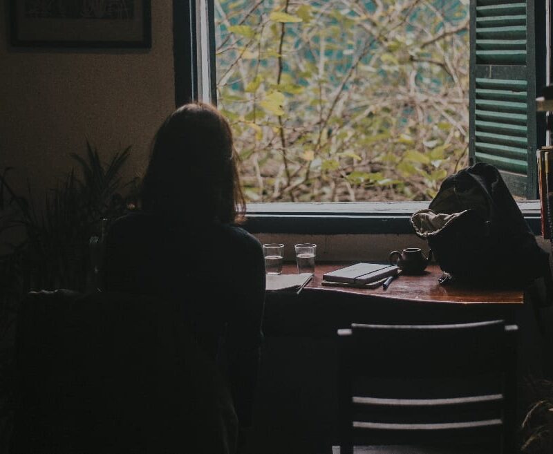 In a dimly lit room, a woman sits near a window symbolizing facts about anorexia, reflecting the isolation and contemplation experienced by many affected individuals.