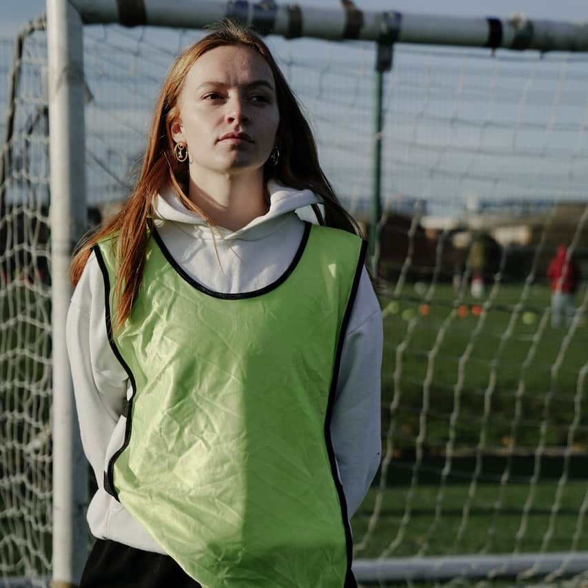 A woman soccer player in uniform, standing on a soccer field, thoughtfully looks off into the distance, symbolizing determination and resilience, relevant to inpatient anxiety treatment centers.