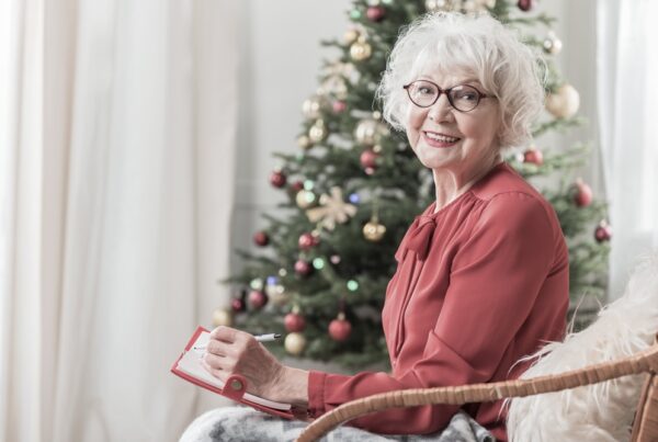 A senior woman seated near the Christmas tree remembering a lost loved one with a smile