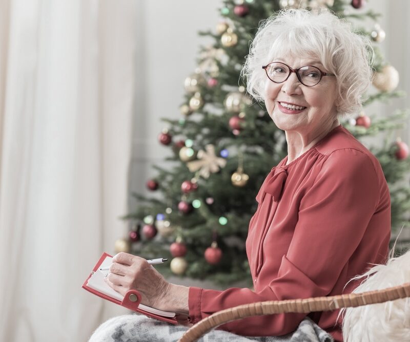 A senior woman seated near the Christmas tree remembering a lost loved one with a smile