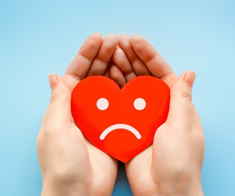 Woman holding a red heart with sad face