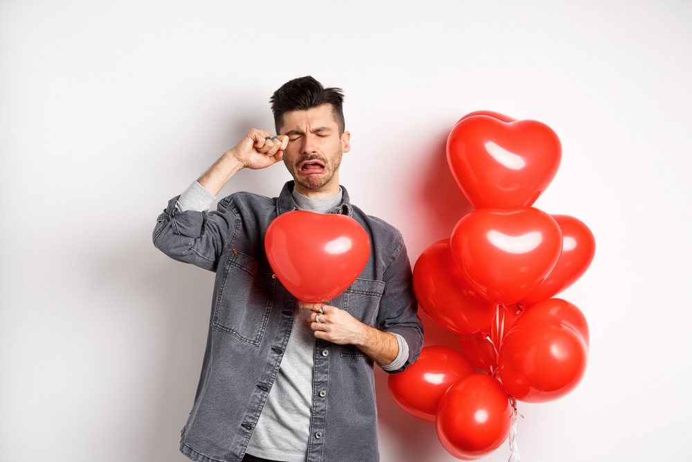 Crying man holding heart-shaped balloons