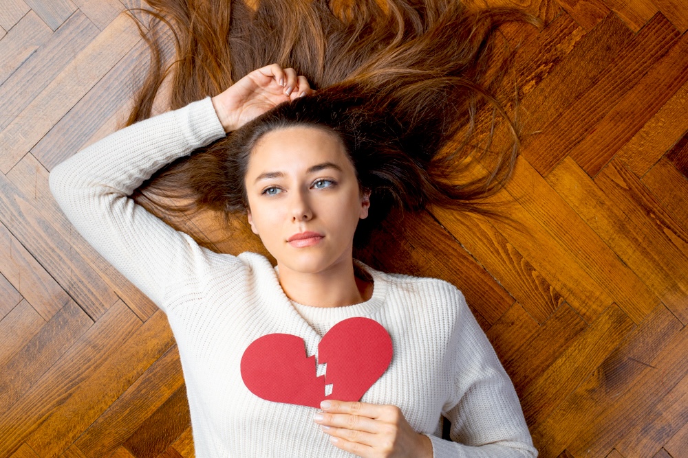 Woman lying on the floor holding a paper broken heart against her chest