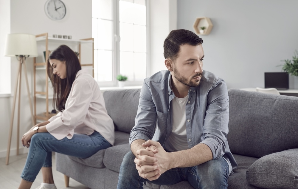 Couple seated at two ends of the couch as one partner with PTSD push the other away